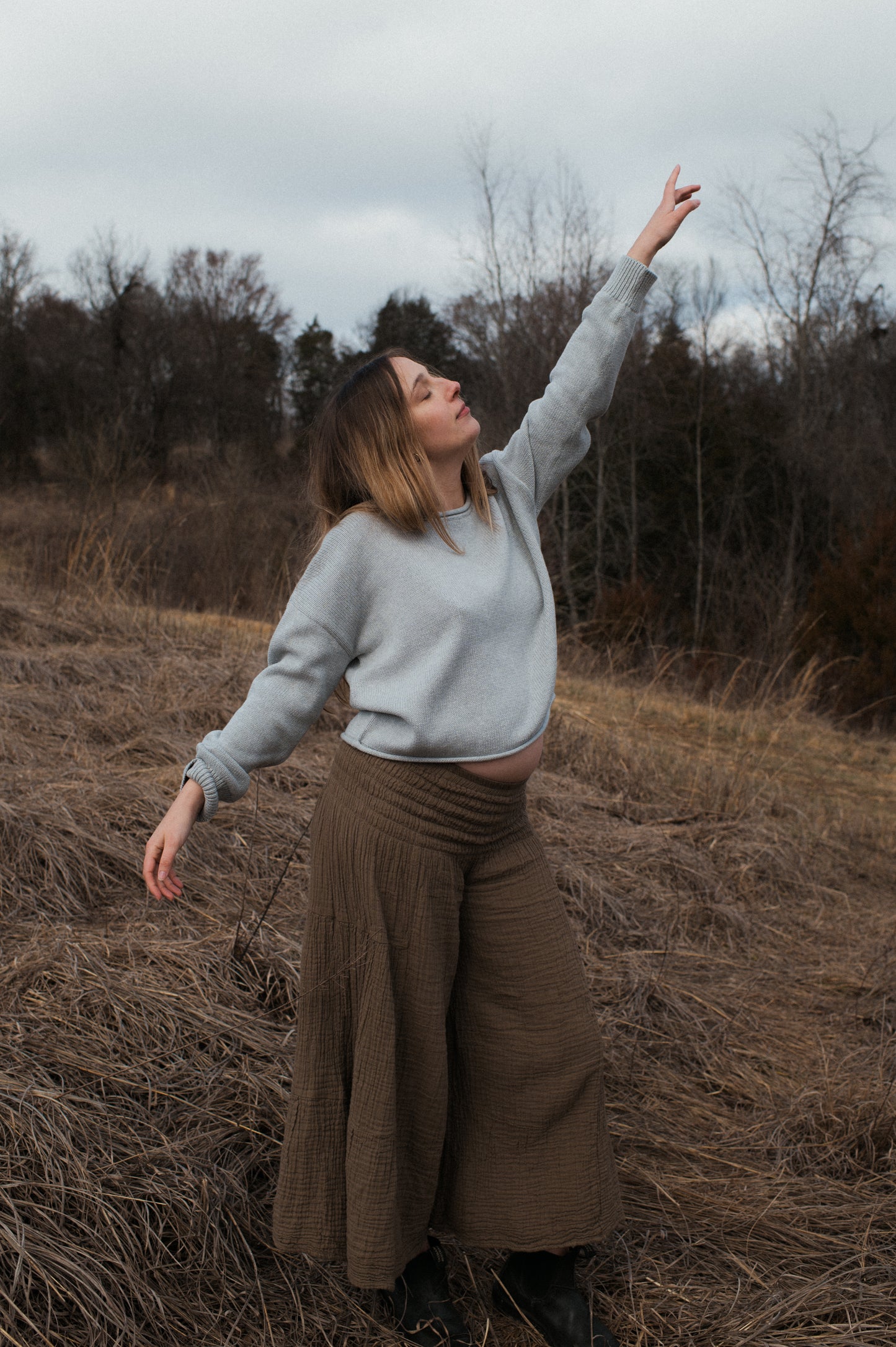 Model pointing to the sky wearing grey true knit cotton sweater.