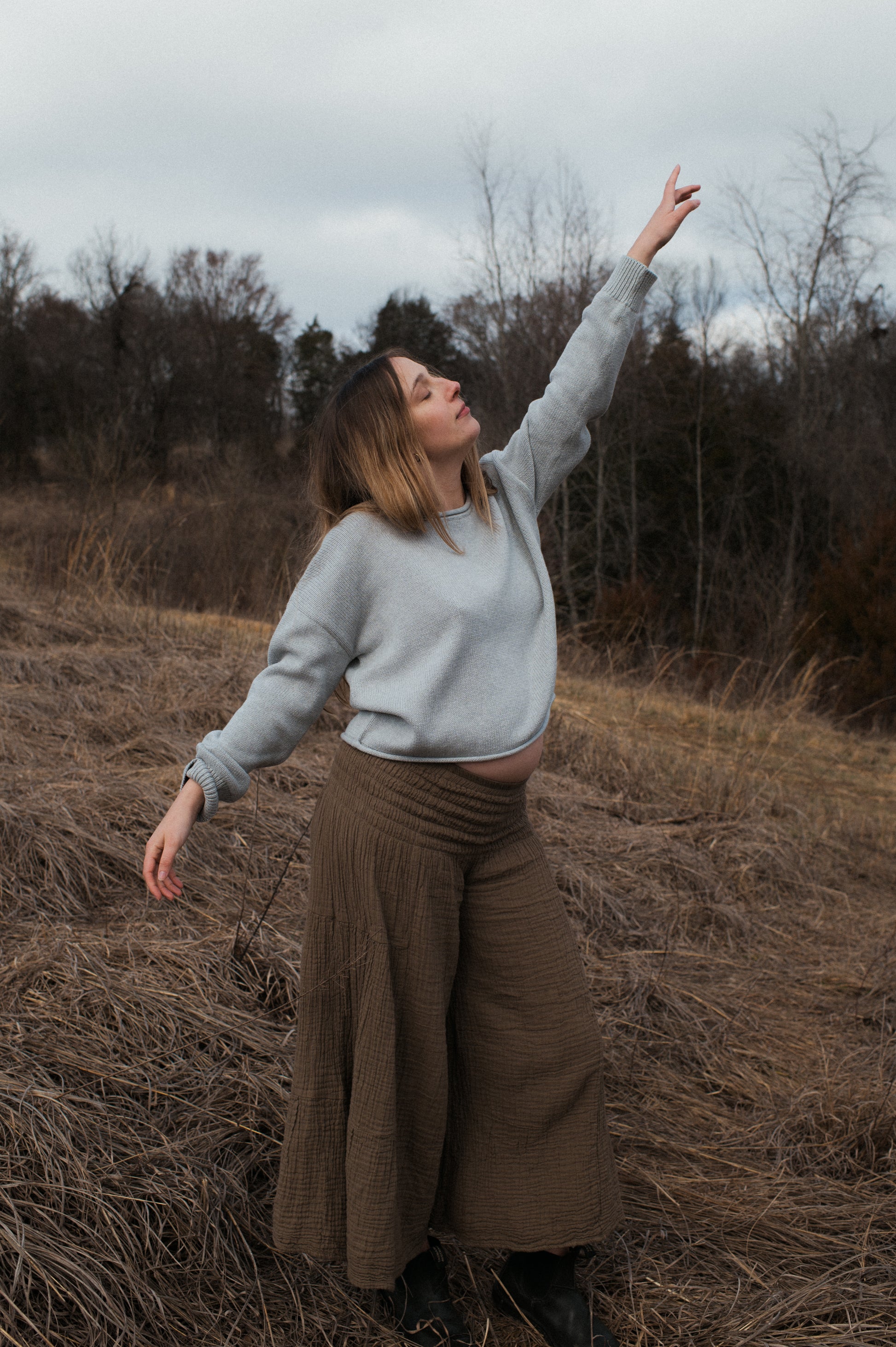 Model pointing to the sky wearing grey true knit cotton sweater.